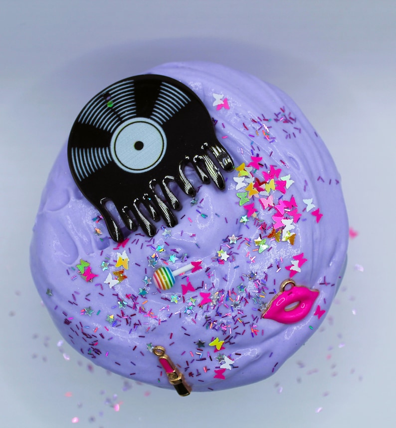 May include: Purple slime with glitter, a black vinyl record, a pink lipstick, a pink lollipop, and pink lips.