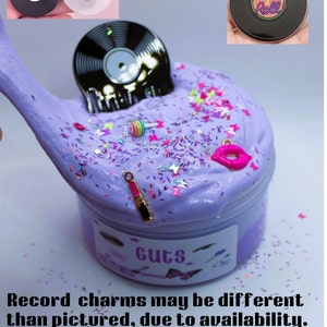 May include: Purple slime with glitter and charms, including a record, lipstick, and a lollipop. The slime is in a clear container with a label that says "Guts".