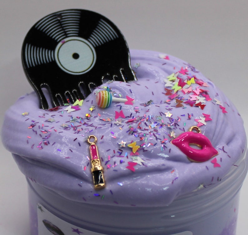 May include: Purple slime with glitter, a black vinyl record, a pink lollipop, a pink lips charm, and a pink lipstick charm.