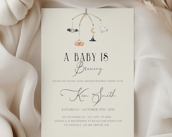 May include: A baby shower invitation with the text "A Baby Is Brewing". The invitation features a decorative mobile with a pumpkin, bat, moon, and witch hat. The invitation is on a cream-colored background with white pumpkins and fabric.
