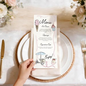 May include: A menu card with ice cream illustrations and text, including "Menu," "Ice Cream," "Toppings," and "Signature Sips." The card is on a white plate with a gold fork and knife, and a floral arrangement in the background.