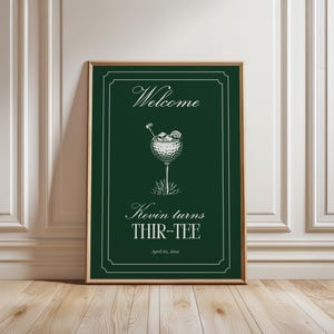May include: A framed print with a dark green background and gold trim. The print features the word "Welcome" at the top, a golf ball cocktail illustration, and the text "Kevin turns THIR-TEE" below. The date "April 01, 20xx" is at the bottom.