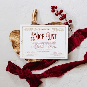 May include: A festive "Nice List" certificate with ornate gold detailing and burgundy text. The certificate, personalized with a name, is set against a white background with a gold leaf and red ribbon. A sprig of red berries adds a holiday touch.