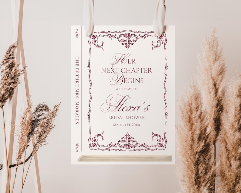 Puede incluir: Un letrero de despedida de soltera con el texto "Her Next Chapter Begins" y "Welcome to Alexa's Bridal Shower". El letrero tiene un borde decorativo burdeos y est&aacute; colgado de una cinta blanca. Tambi&eacute;n est&aacute; presente el texto "The Future Mrs. Morales".
