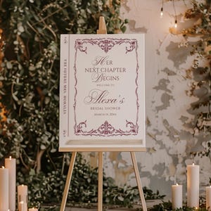 May include: A white welcome sign for a bridal shower, displayed on an easel. The sign features burgundy text and decorative borders. It reads "Her Next Chapter Begins" and welcomes guests to Alexa's bridal shower on March 14, 20XX. The words "The Future Mrs. Morales" are on the side.