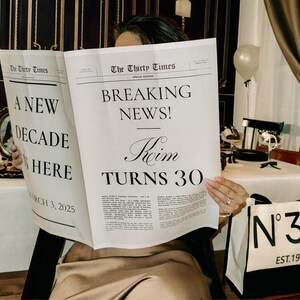 K&ouml;nnte beinhalten: Eine Frau h&auml;lt eine Zeitung mit der Schlagzeile "Breaking News! Roim Turns 30" und dem Text "A New Decade is Here" auf der linken Seite. Sie h&auml;lt eine wei&szlig;e Tragetasche mit schwarzem Besatz und dem Text "N&deg;30 EST. 1995" auf der Vorderseite.