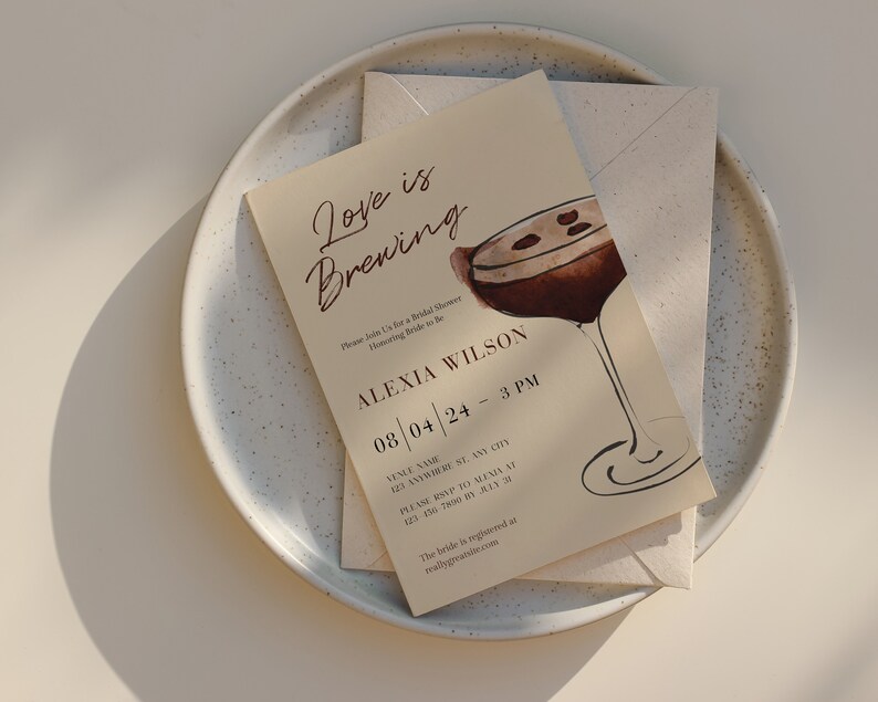 Puede incluir: Una invitaci&oacute;n beige para una despedida de soltera con el texto "Love is Brewing" y una ilustraci&oacute;n de acuarela de un c&oacute;ctel. La invitaci&oacute;n incluye detalles del evento, como la fecha, la hora y el lugar, y est&aacute; colocada sobre un plato moteado.