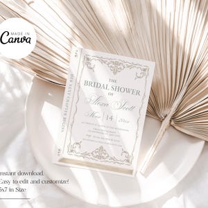 May include: A bridal shower invitation in a book-like design. The invitation is white with gold-colored decorative elements and text. The text reads "The Bridal Shower of Alexa Scott" and includes the date, March 14, 2022. The invitation is 5x7 inches.