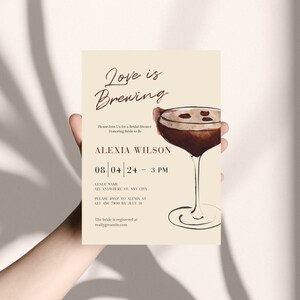 Puede incluir: Una invitaci&oacute;n a una despedida de soltera con el texto "Love is Brewing" en una elegante escritura. La invitaci&oacute;n presenta una ilustraci&oacute;n de acuarela de un c&oacute;ctel e incluye detalles para la despedida de soltera de Alexia Wilson.