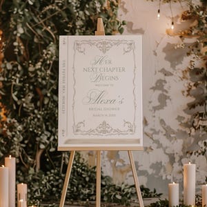 Puede incluir: Un letrero blanco sobre un caballete de madera con el texto "Her Next Chapter Begins" y "Alexa's Bridal Shower". El letrero tiene bordes decorativos y est&aacute; rodeado de velas y vegetaci&oacute;n, creando un ambiente festivo.
