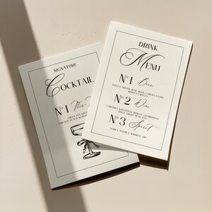 May include: Two white cards with black text and borders. The card on the left has the text "SIGNATURE COCKTAIL" and "N°1 The ..." The card on the right has the text "DRINK MENU" and "N°1 Beer", "N°2 Wine", and "N°3 Spirit".