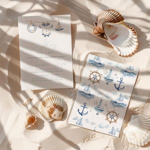 May include: Baby shower invitation with nautical theme. The invitation features the text "Ahoy It's a Boy" and a watercolor illustration of a sailboat, life preserver, and baby clothes. A patterned card with sailboats, anchors, and steering wheels is also present.