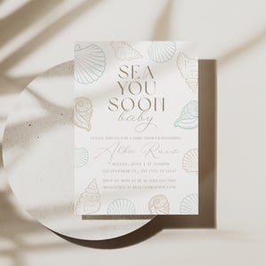 Może przedstawiać: Zaproszenie na baby shower z motywem muszli. Tekst "Sea You Soon baby" jest wyświetlany stylową czcionką. Zaproszenie zawiera szczeg&oacute;ły takie jak data, godzina i miejsce, wraz z imieniem "Alba Ruiz".