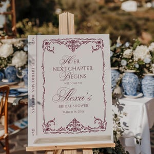Puede incluir: Un letrero blanco sobre un caballete con el texto "Her Next Chapter Begins" en escritura burdeos, dando la bienvenida a los invitados a la despedida de soltera de Alexa. El letrero est&aacute; decorado con bordes ornamentados y la fecha 14 de marzo de 20xx. Las palabras "The Future Mrs. Morales" est&aacute;n impresas verticalmente en el lateral.