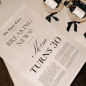 K&ouml;nnte beinhalten: Eine Zeitungs&uuml;berschrift mit der Aufschrift "Breaking News!" und dem Text "Kim Turns 30" in einer stilisierten Schriftart. Die Zeitung liegt auf einem Tisch mit einer Weinflasche und einem Glas.