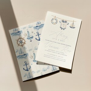May include: Baby shower invitations with a nautical theme. The invitations feature watercolor illustrations of sailboats, anchors, and a ship's wheel. One invitation reads "Ahoy It's a Boy" with event details. The design includes a watercolor illustration of a baby onesie, a life preserver, and a sailboat.