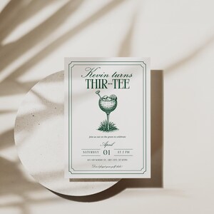 K&ouml;nnte beinhalten: Eine wei&szlig;e Einladungskarte mit gr&uuml;nem Text und einer Golf-Illustration. Der Text lautet "Kevin turns THIR-TEE" mit Veranstaltungsdetails. Die Karte liegt auf einer wei&szlig;en, kreisf&ouml;rmigen Oberfl&auml;che mit Schatten.