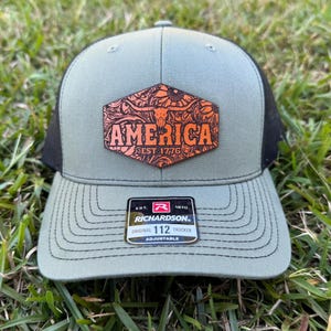 May include: A green and black trucker hat with a patch that reads "AMERICA EST. 1776". The patch has an orange floral design with a bull skull. The hat is adjustable and has a Richardson tag.