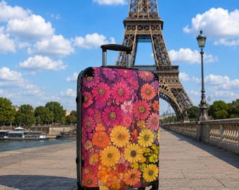 May include: A rolling suitcase featuring a vibrant floral pattern with numerous daisy-like flowers in shades of pink, orange, and yellow. The luggage has a black frame, a retractable handle, and four wheels, standing upright on a paved walkway.