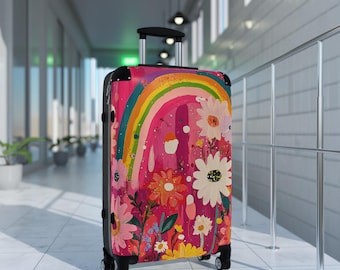 May include: A rolling suitcase with a vibrant floral and rainbow design. The luggage features a pink background with colorful flowers and a rainbow arching across the top. The suitcase has a black frame and handle.