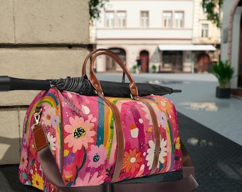 May include: A colorful duffel bag with a floral and rainbow design. The bag features a pink background with various flowers in shades of pink, yellow, and white. It has brown leather handles and a detachable shoulder strap. An umbrella rests on top.