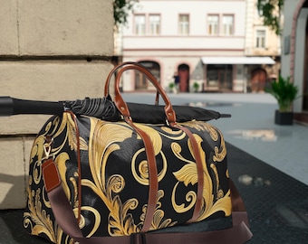 May include: A black and gold patterned duffel bag with brown leather handles and straps. The bag has a decorative floral design and a detachable shoulder strap. An umbrella rests on top of the bag.