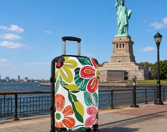 May include: A rolling suitcase with a white base featuring a vibrant floral pattern in shades of red, orange, yellow, and green. The luggage has a black frame, a retractable silver handle, and four black wheels, standing upright on a paved walkway.