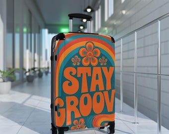 May include: A rolling suitcase featuring a teal background with orange and yellow rainbow arches and flower motifs. The text STAY GROOV is printed in large, bold orange letters across the center. It has a black handle and four wheels.