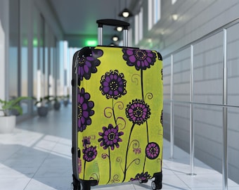 May include: A green suitcase with a floral pattern featuring purple and black flowers. The suitcase has a black handle and wheels.