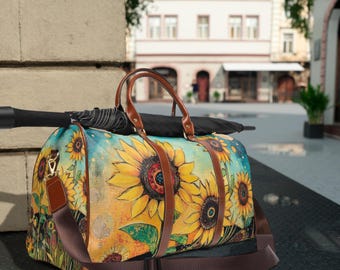 May include: A duffel bag with a vibrant sunflower design. The bag features large yellow sunflowers with brown centers against a blue and yellow background. It has brown leather handles and a detachable shoulder strap. An umbrella rests on top.