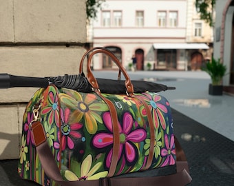 May include: A floral print duffel bag with brown leather accents and a long adjustable shoulder strap. The bag has a colorful design with pink, yellow, green, and blue flowers on a black background.