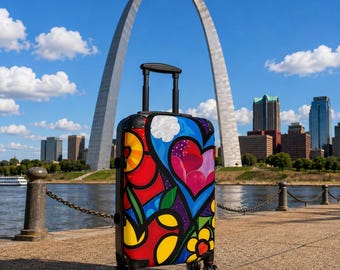 May include: A hard-shell rolling suitcase featuring a vibrant, multi-colored abstract design with bold black outlines, heart shapes, and floral patterns. The luggage has a black retractable handle, four spinner wheels, and a sturdy rectangular frame.