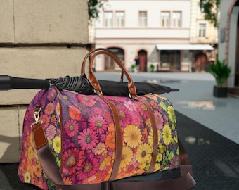 May include: A floral print duffel bag with brown leather accents and a long brown strap. The bag is sitting on a black surface.