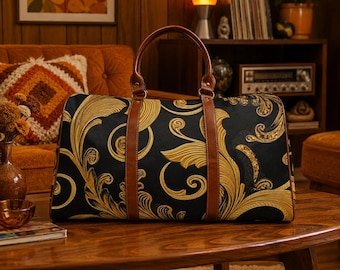 May include: A duffel bag featuring a black fabric base with a gold-colored swirling acanthus leaf pattern. The bag includes two brown leather-like handles and matching brown vertical straps that extend from the top to the bottom of the bag.