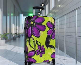 May include: A green suitcase with a purple and black floral pattern. The suitcase has a retractable handle and four wheels.