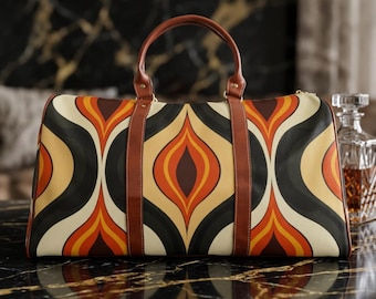May include: A duffel bag featuring a repeating geometric pattern in shades of orange, yellow, cream, and black. The bag has two brown leather handles and brown leather vertical straps that extend from the top handles down to the base.