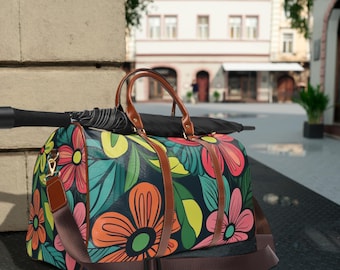 May include: A floral print duffel bag with brown leather handles and straps. The bag features a colorful pattern of large flowers in shades of pink, orange, and yellow against a dark background. An umbrella rests on top of the bag.