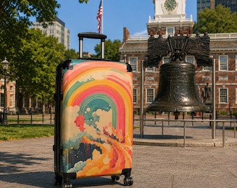 May include: A hard-shell rolling suitcase featuring a vibrant, multi-colored graphic print of a rainbow arching over stylized clouds and abstract shapes. The luggage has a black frame, a retractable silver handle, and four black spinner wheels.
