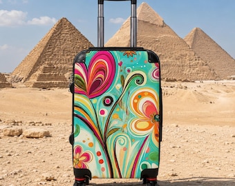 May include: A rolling suitcase with a retractable handle and black trim, featuring a vibrant, multi-colored abstract floral pattern in shades of teal, pink, orange, and yellow. The luggage stands upright on four black wheels against a desert landscape.