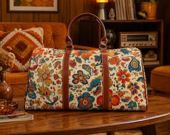 May include: A rectangular duffel bag featuring a cream-colored base with a vibrant, multi-colored floral and paisley pattern in shades of orange, red, blue, and yellow. The bag includes two brown leather handles and matching brown leather trim.