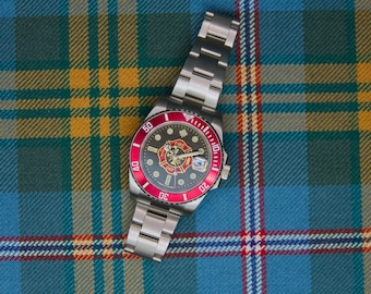 May include: A stainless steel wristwatch with a silver link band, a red rotating bezel with white numerals, and a black dial featuring a central Fire Department emblem with gold and red details, white hour markers, and a date window.