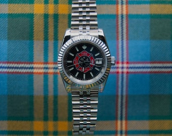 May include: A silver-tone stainless steel wristwatch featuring a fluted bezel and a jubilee-style link bracelet. The black dial displays a red and black fire department emblem at the center, a date window at the three o'clock position, and a small maple leaf.