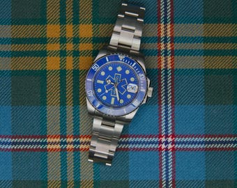 May include: A stainless steel wristwatch with a blue rotating bezel and a blue dial featuring a yellow Star of Life medical emblem. The watch has a date window at the three o'clock position, luminous hour markers, and a silver-toned metal link bracelet.