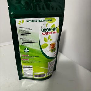 Puede incluir: Una bolsa verde con una etiqueta blanca que dice "Organic Soursop Tea" y enumera los beneficios y ventajas del té. La bolsa está sobre una superficie blanca.