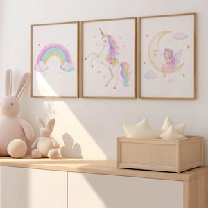 May include: Three framed wall art prints featuring watercolour illustrations. The left print shows a rainbow with clouds, the centre print depicts a unicorn with a floral mane, and the right print shows a fairy sitting on a crescent moon.