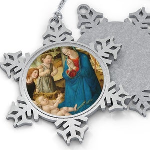 Puede incluir: Adorno de copo de nieve plateado con una imagen redonda de la Natividad. La imagen representa a María, José y el niño Jesús. El adorno tiene una cuerda plateada para colgar.