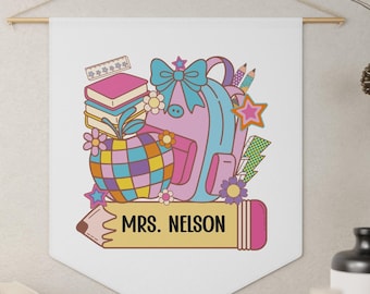 Pode incluir: Uma tapeçaria de parede branca com um design com tema escolar. O design inclui uma mochila, livros, lápis e o texto "MRS. NELSON" em uma faixa em forma de lápis. A obra de arte apresenta um estilo retrô colorido.