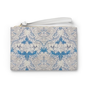 May include: A white clutch purse with a blue floral pattern and a gold zipper. The purse has a white strap.