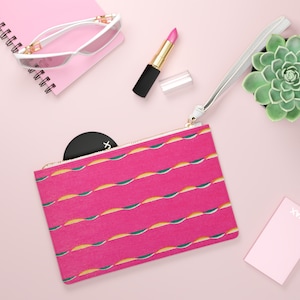 May include: A pink zippered pouch with a white zipper and a green and yellow wavy pattern. The pouch is lying on a pink surface with a small round mirror, a pink lipstick, and a small succulent plant in a white pot.