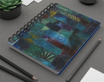 Puede incluir: Un cuaderno de espiral con una pintura abstracta azul, verde y amarilla en la portada. La pintura recuerda a una ciudad con formas geométricas y líneas.